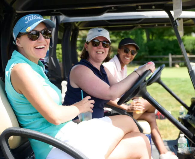three women smiling in a golf cart at event