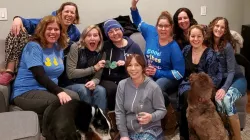 A colorectal cancer advocate is surrounded by friends, family, and two dogs on a couch, having a fun time together