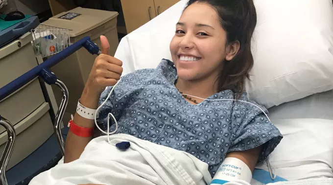 Woman in hospital bed giving thumbs up
