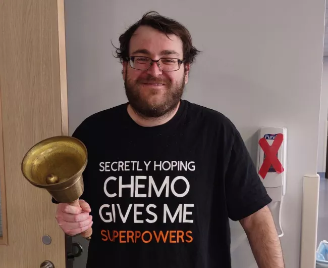 Gabriel Leblanc rings a bell while wearing a shirt that says, "Secretly hoping chemo gives me superpowers."